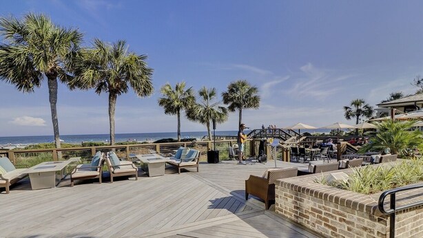 A wooden deck with lounge chairs and a brick wall, overlooking the ocean with palm trees. - Sunset Rentals | South Live Oak 25 (Hilton Head Island)