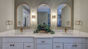 A bathroom with two sinks, a large mirror, and a plant centerpiece. - Sunset Rentals | South Live Oak 25 (Hilton Head Island)