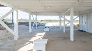 Une construction située au bord de la plage, dotée d’un plancher en béton et de poutres blanches, et comprenant une porte et un banc.