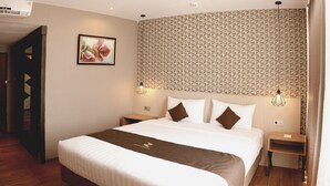 Quarto de hotel com cama grande, piso de madeira, ar condicionado fixado na parede, quadro emoldurado e parede com padrão geométrico.