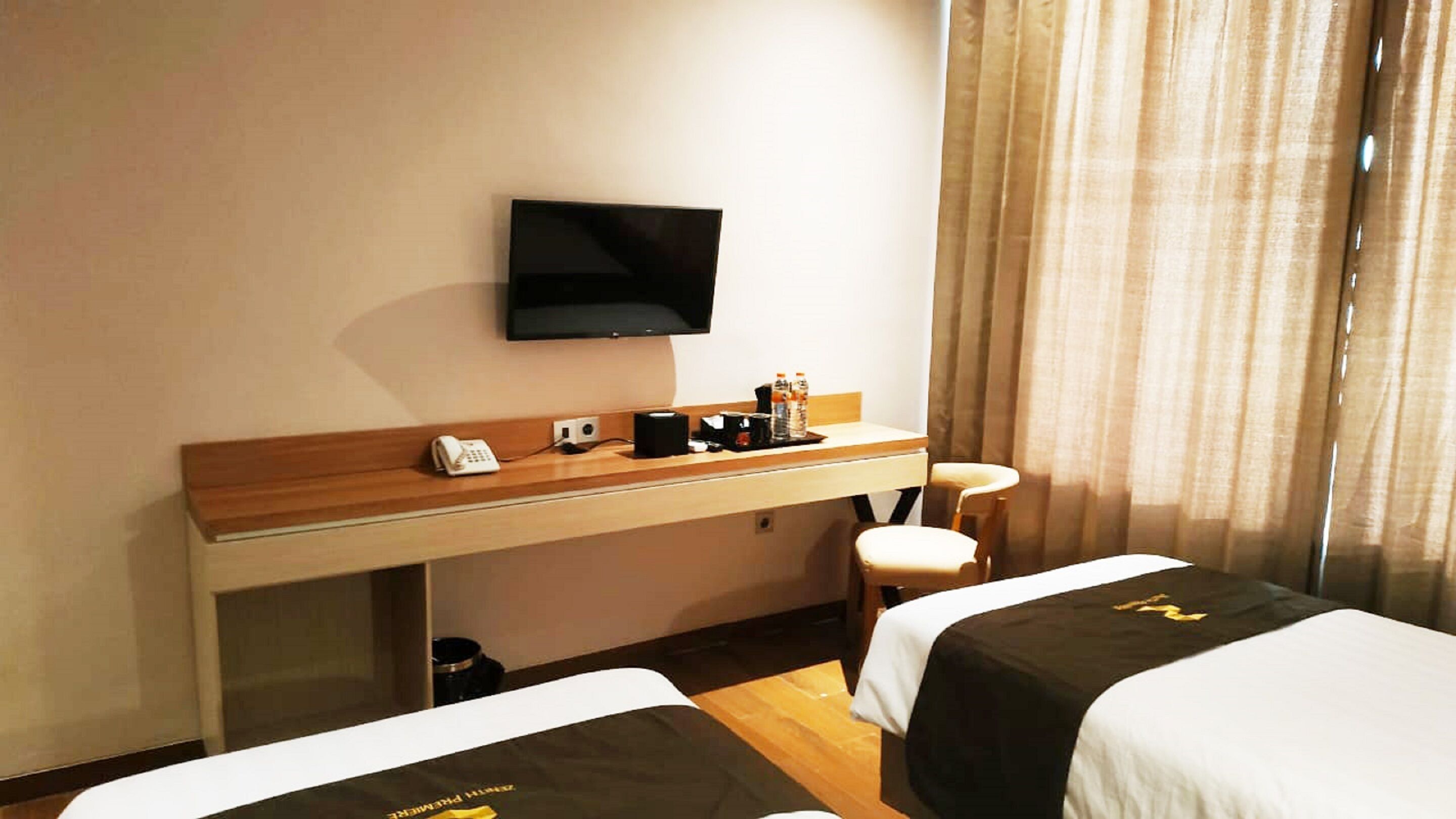 A hotel room with a desk, a television, a chair, and two beds.