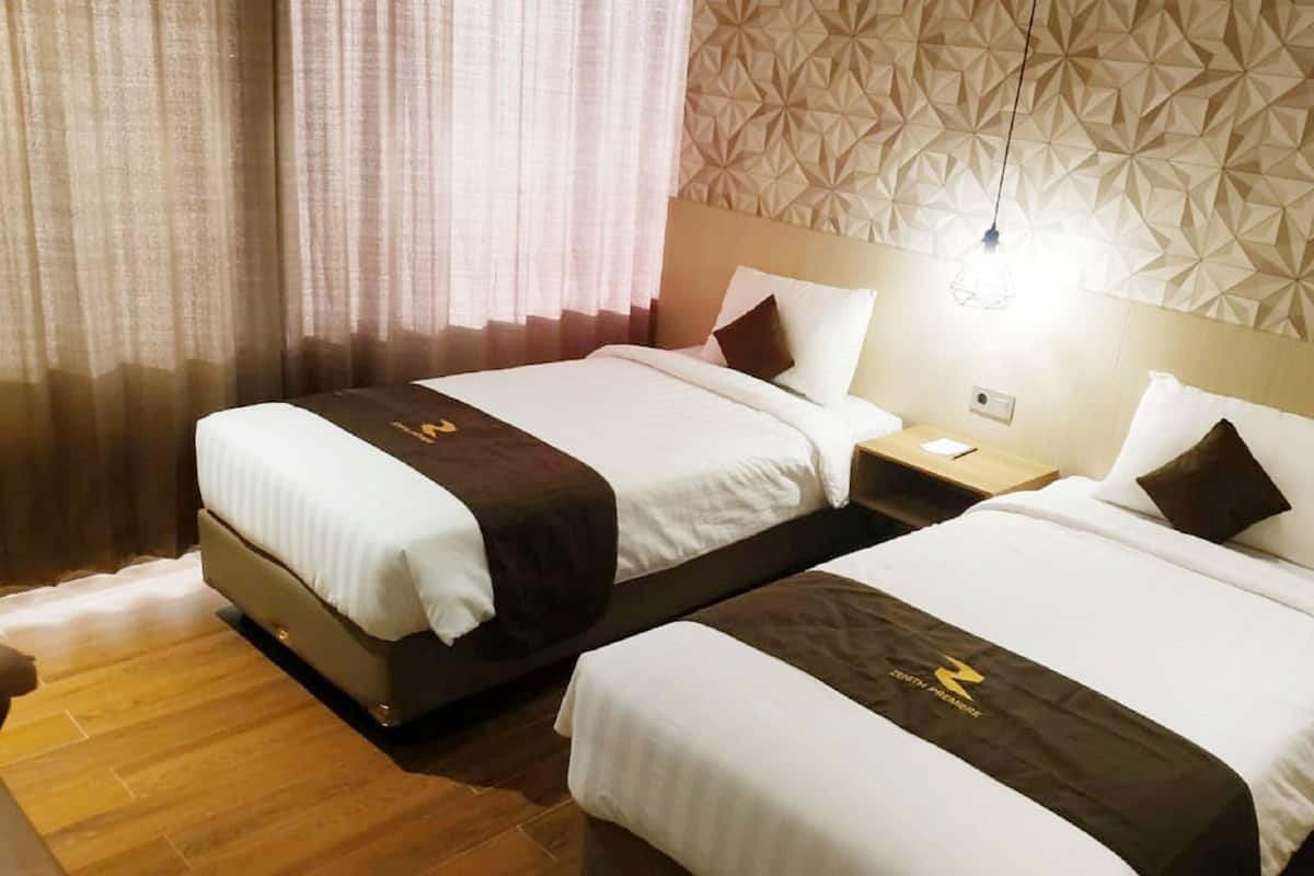 A hotel room with two beds, a wooden floor, a patterned wall, and a nightstand with a lamp.