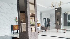 Um lobby moderno com piso de mármore, balcão de recepção, área de estar e um lustre decorativo.