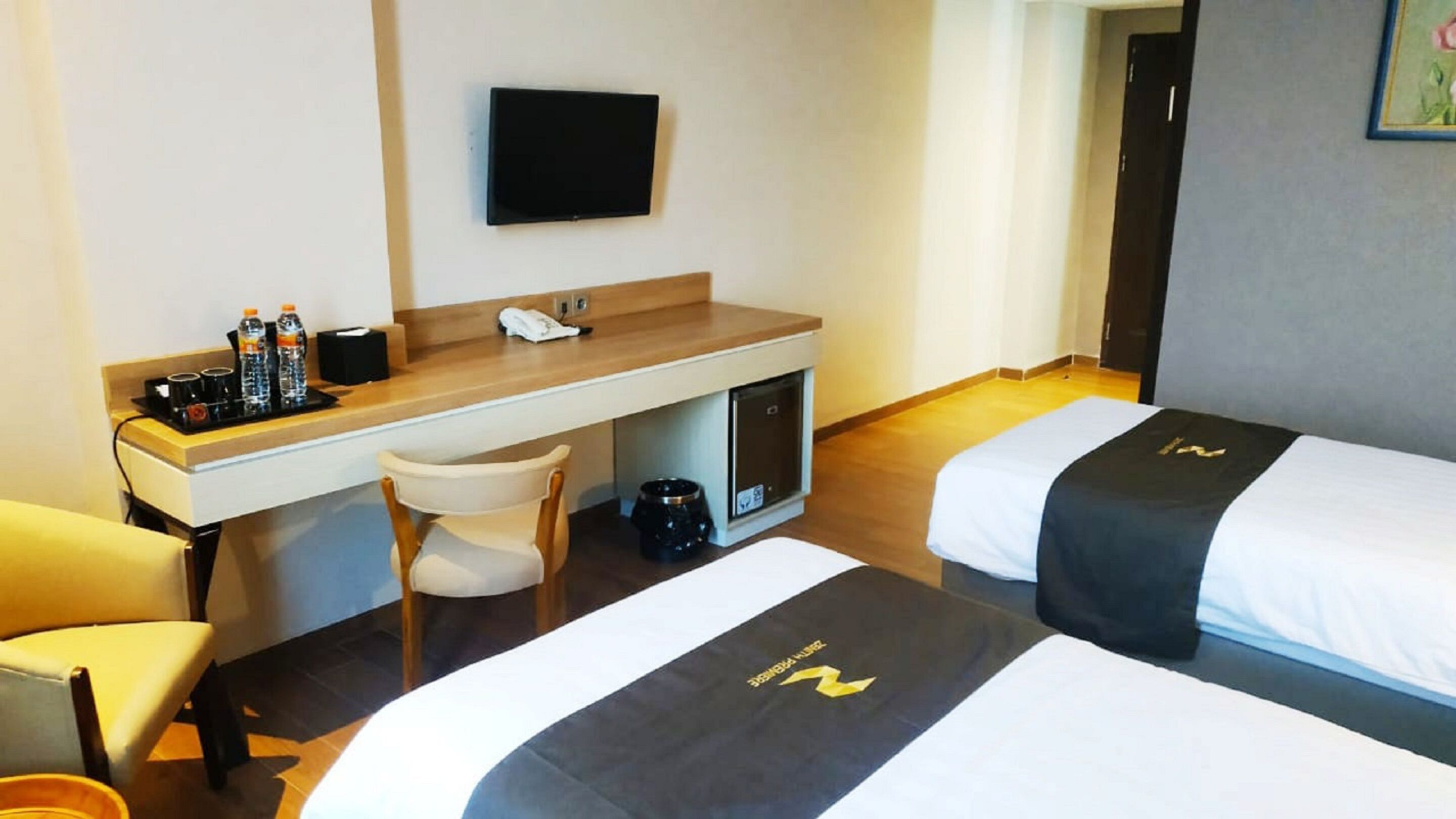 A hotel room with two beds, a desk, a chair, and a television.