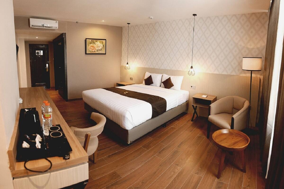 A hotel room with a bed, bedside tables, a desk with a chair, a lamp, and a wooden floor.