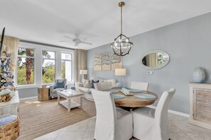 Ein modernes Wohnzimmer mit Essbereich, großen Fenstern, Deckenventilator und Kunstwerken an den Wänden.