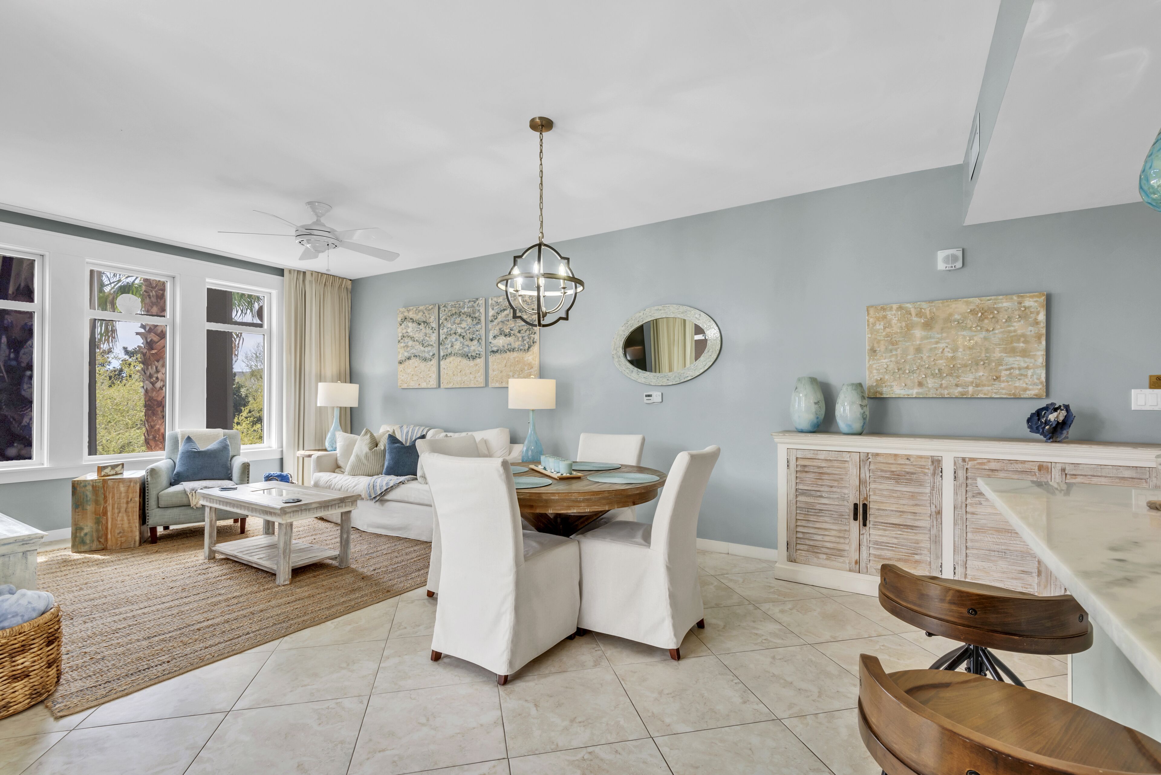 A spacious living room with a round coffee table, white cushioned chairs, a ceiling fan, and a dining area with a wooden table and chairs.
