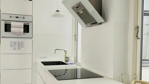 A modern kitchen with white cabinetry, a black induction cooktop, a stainless steel range hood, and pendant lighting. - City Apartment in Copenhagen with 2 bedrooms sleeps 6 (Copenhagen)