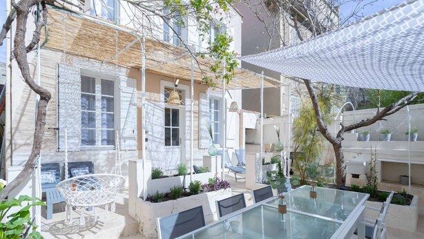 A modern outdoor seating area with a glass table and chairs, surrounded by potted plants and a white fence. - MaisonMars La Maison de Famille (Marseille)