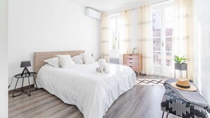 A modern bedroom with a large bed, a bedside table with a lamp, a dresser, and a window with curtains. - MaisonMars La Maison de Famille (Marseille)