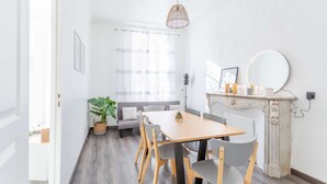 A bright, modern dining area with a wooden table and chairs, a white fireplace, and a large mirror. - MaisonMars La Maison de Famille (Marseille)