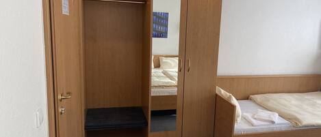Een houten garderobe met spiegel, een bed met matras en kussens, en een klein opstapje naar de garderobe.