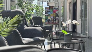 A modern indoor seating area with black upholstered chairs, a round black table with a potted orchid, and a glass wall with a view of greenery and a bookstore. - Mirage City Hotel Stuttgart (Stuttgart)