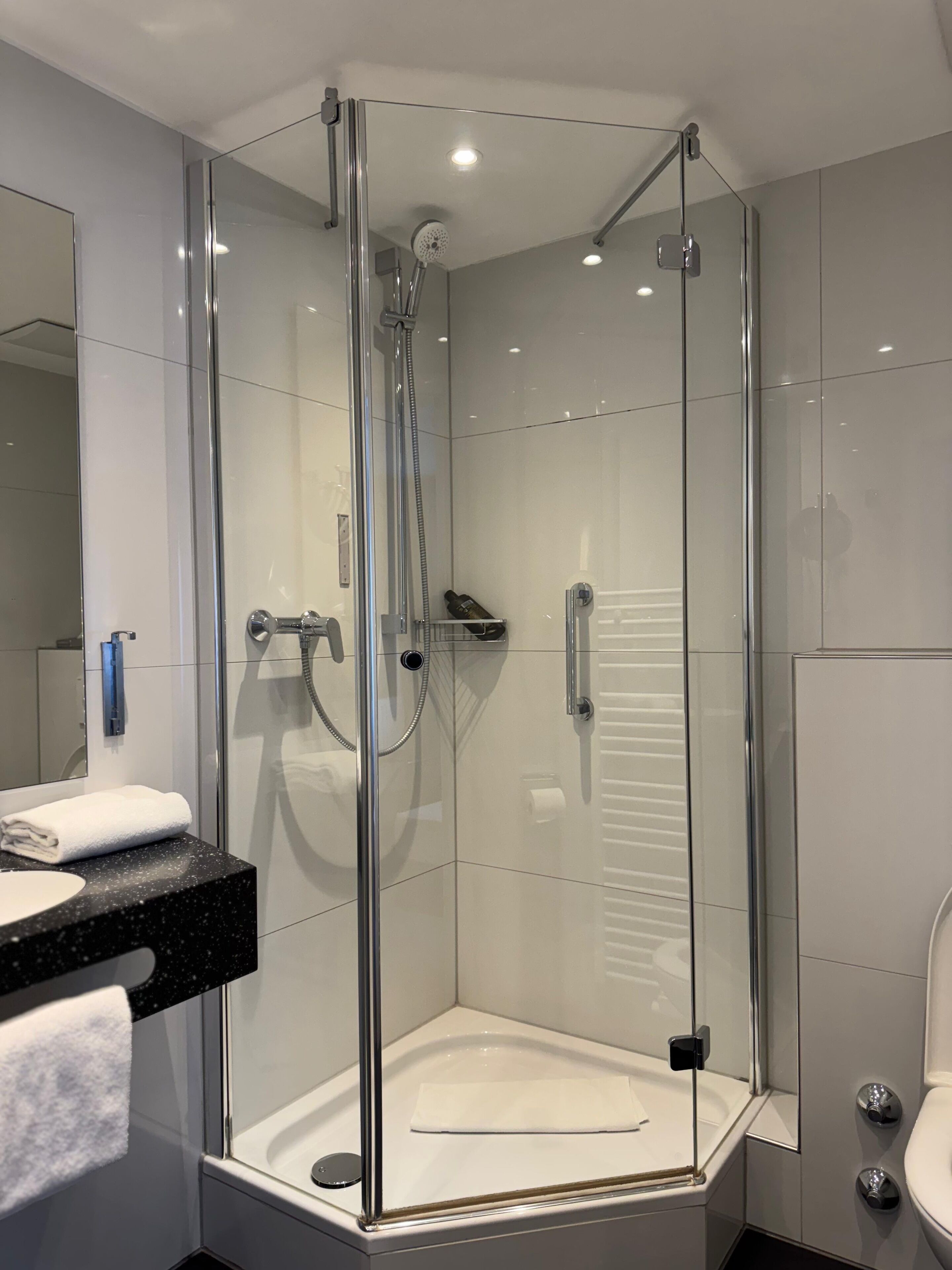 A modern bathroom with a glass-enclosed shower, a white sink with a black countertop, and a toilet.