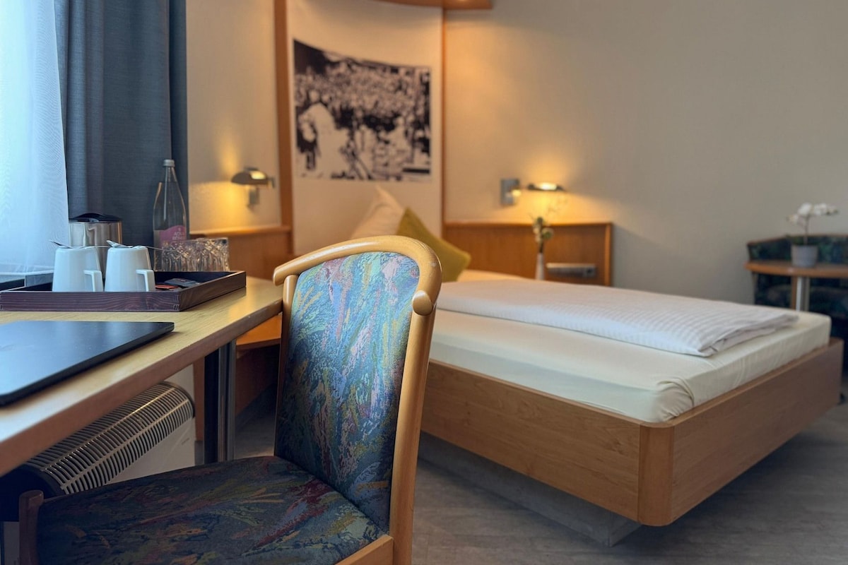 Hotellihuone, jossa on sänky, työpöytä, tuoli ja seinälle ripustettu taulu.