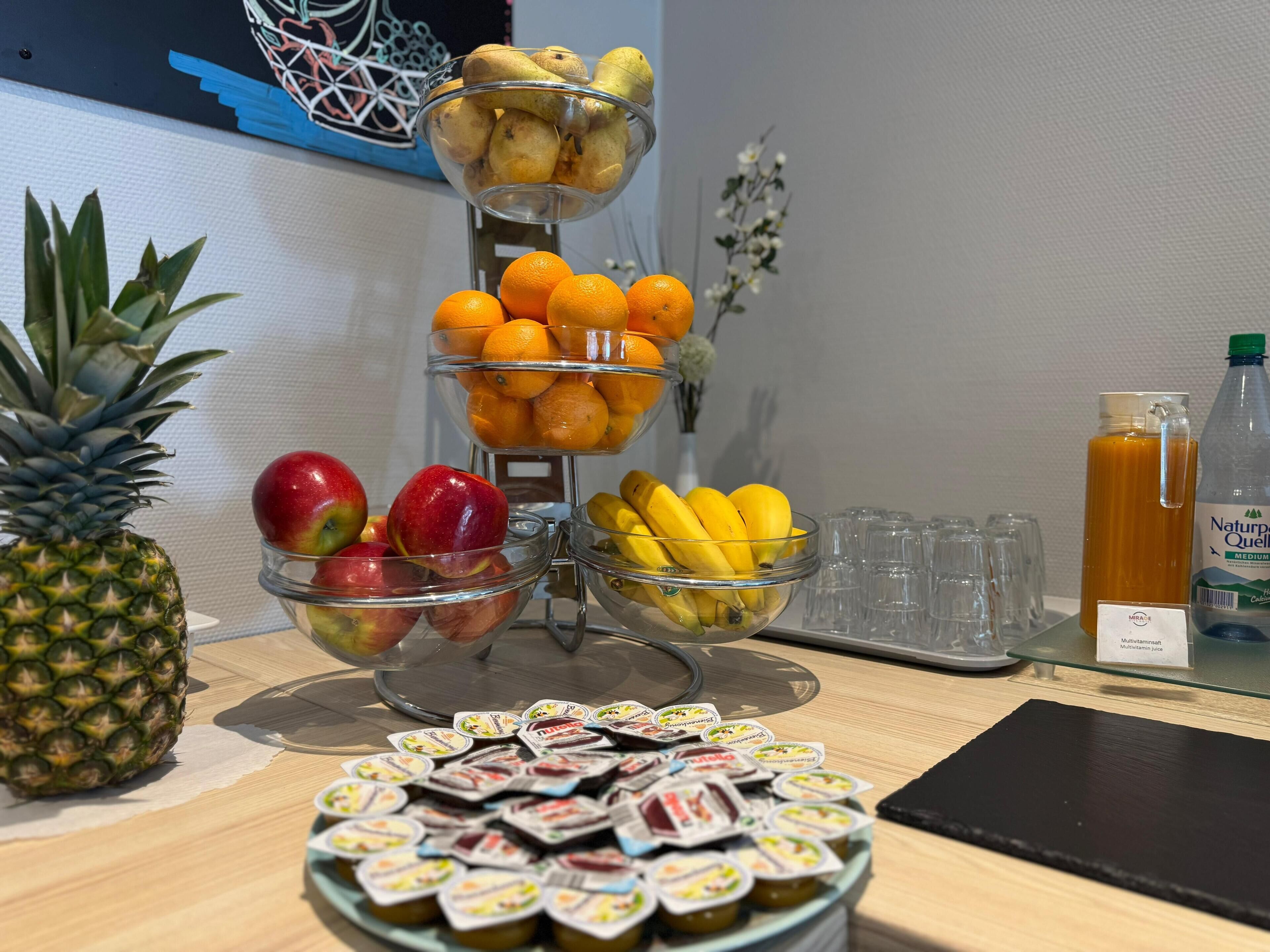 A fruit and juice display with a pineapple, apples, oranges, bananas, and a bottle of juice.