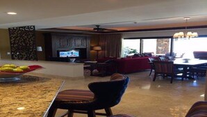 A modern living room with a TV, a dining area with chairs, and a kitchen island with fruit. - 2Bedroom 3Bath Ocean Presidential Unit (Cabo San lucas)