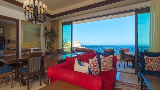 A spacious living room with a red sofa, a dining area, and a balcony with a view of the sea. - 2Bedroom 3Bath Ocean Presidential Unit (Cabo San lucas)