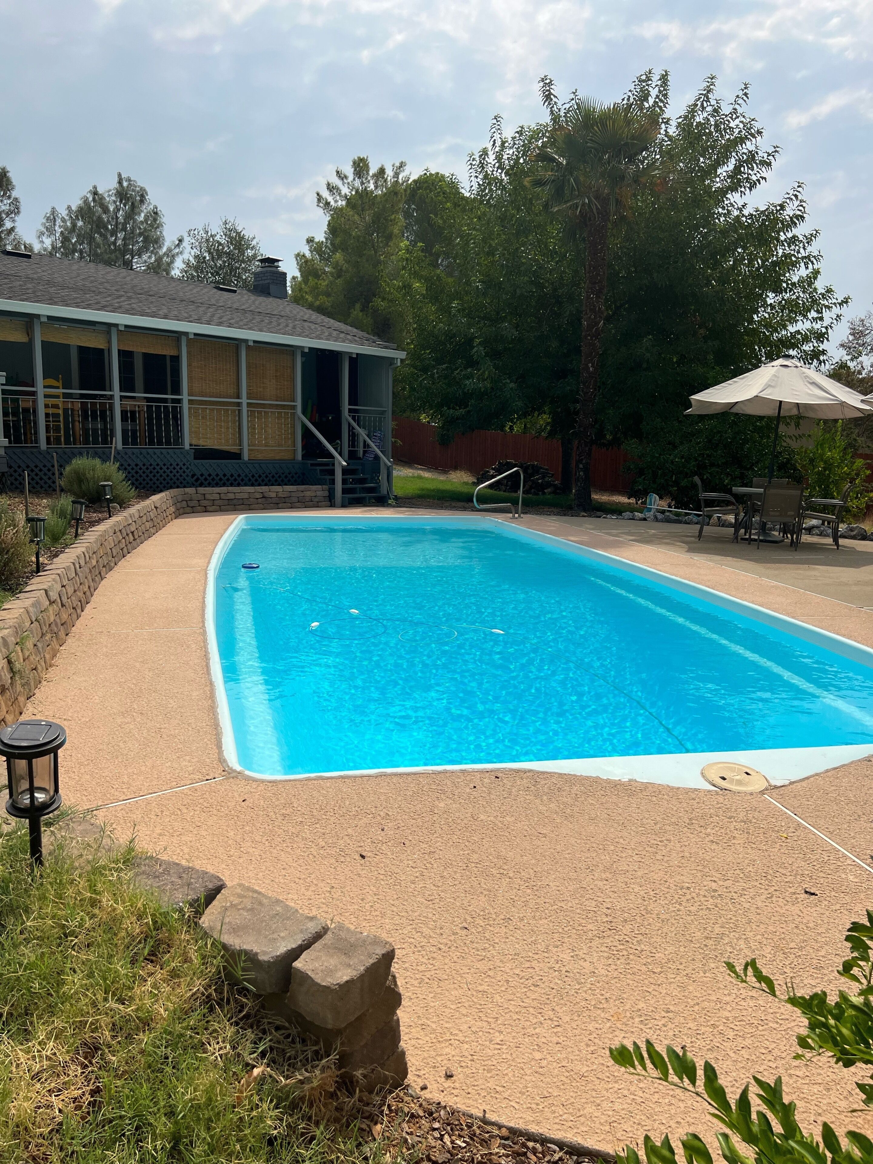 A rectangular swimming pool with a clear blue water, surrounded by a concrete deck.
