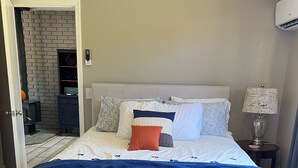 Quarto com cama, mesa de cabeceira, luminária e parede com padrão de tijolos.