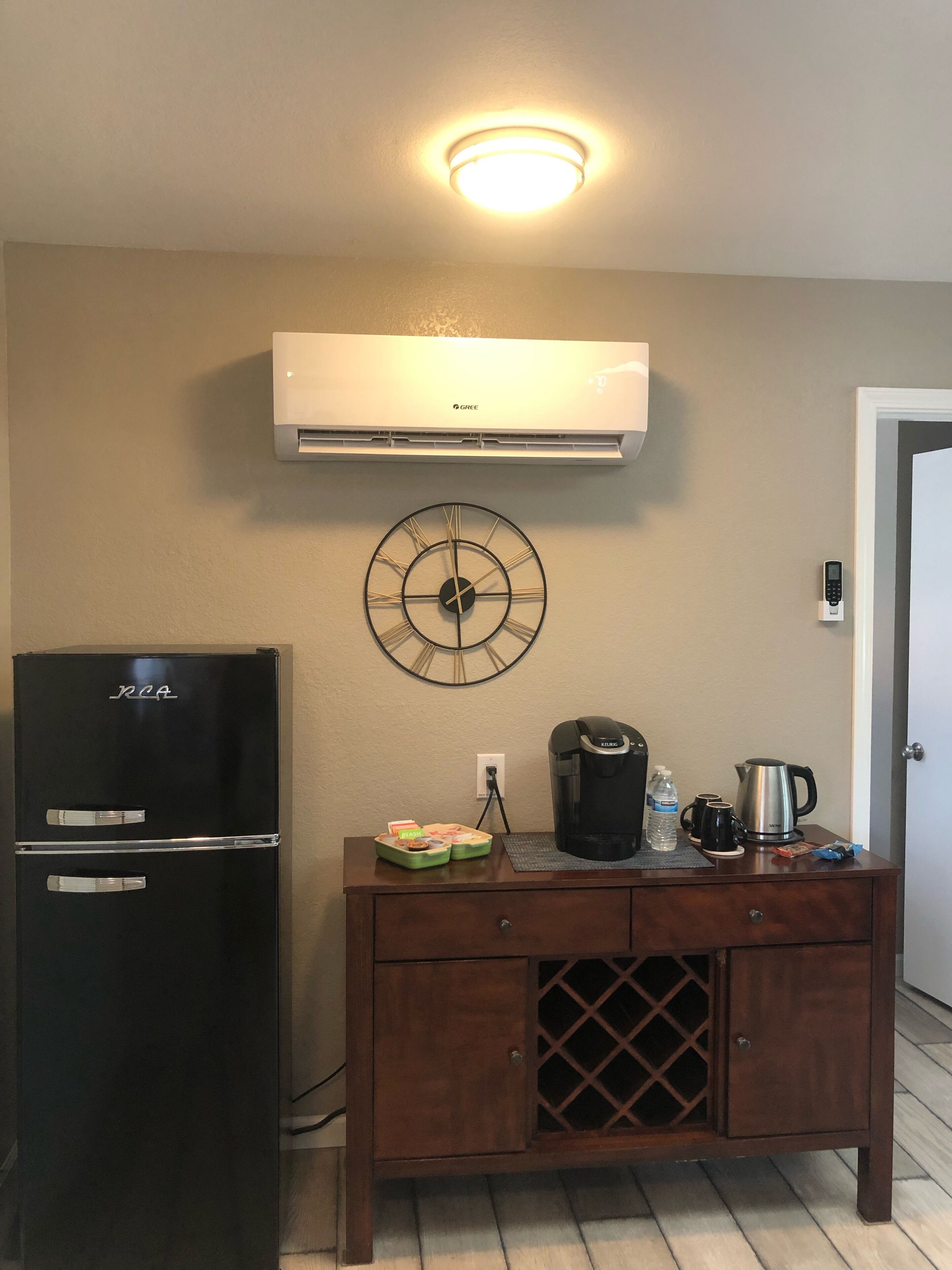 A kitchenette with a black refrigerator, a coffee maker, and a clock on the wall.