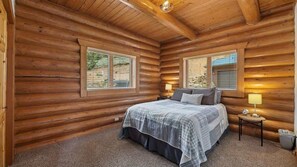A log cabin bedroom with a bed, two bedside tables, and a window. - Last Resort (Red Lodge)