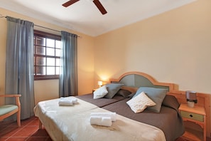 Ein Hotelzimmer mit einem Bett, einem Sessel, einem Nachttisch, einer Lampe und einem Fenster mit Vorhängen.