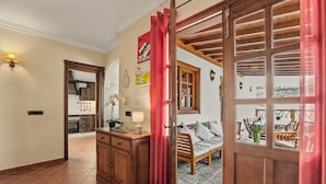 A room with a wooden wardrobe, a bed with a view, a red curtain, and a tiled floor.