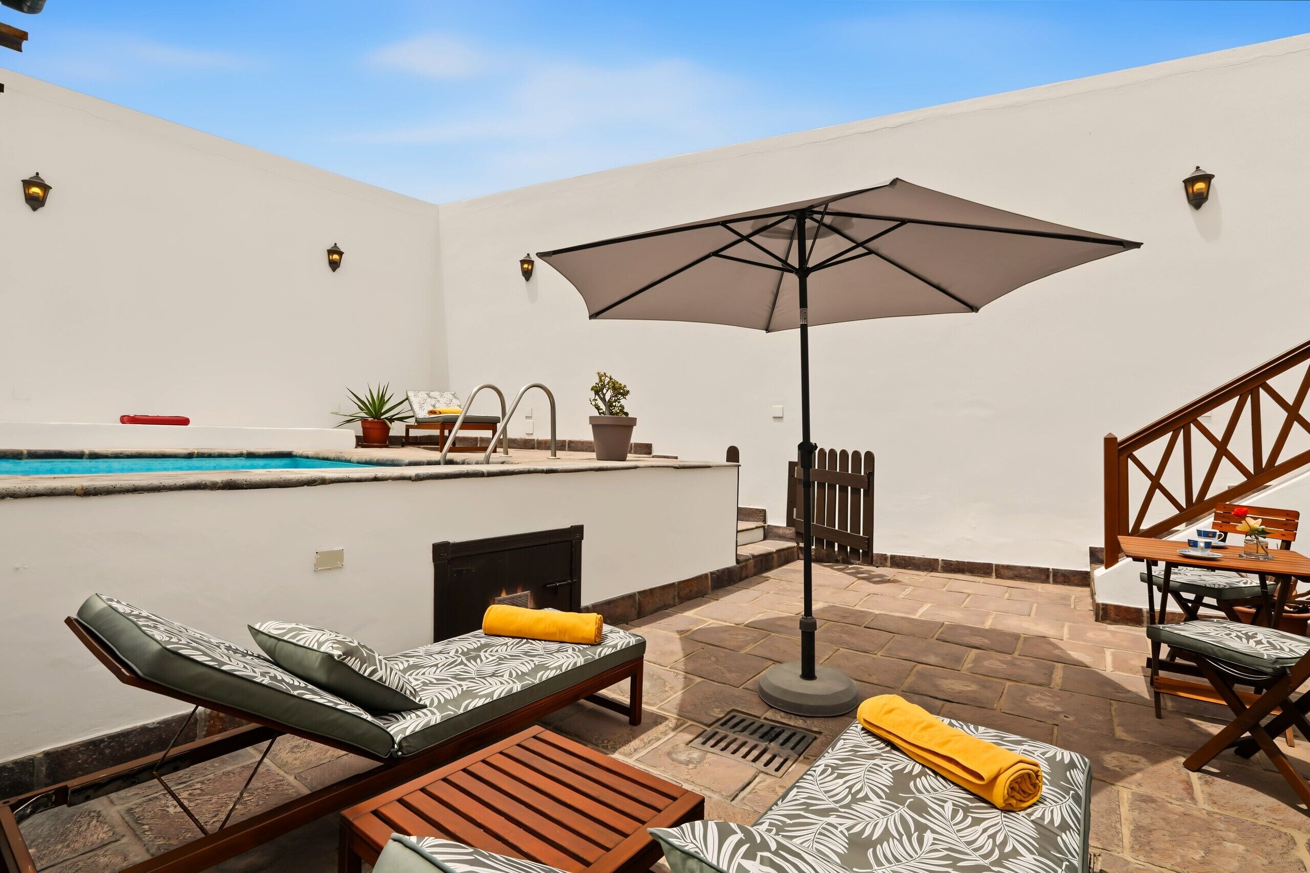 Een zwembadterras met ligbedden, een tafel, een parasol en een trap.
