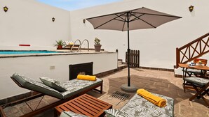 A poolside area with lounge chairs, a table, an umbrella, and a staircase.