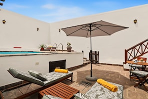 Un espace aménagé au bord de la piscine, avec des chaises longues, une table, un parasol et un escalier.