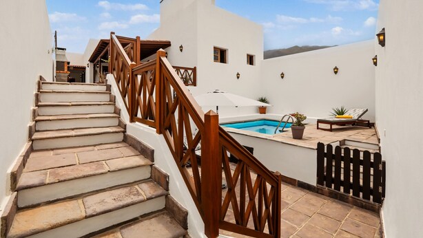 A staircase leading to a rooftop area with a pool, a wooden railing, and a view of the sky.