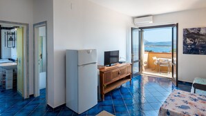 A room with a kitchen, a refrigerator, a television, a wooden cabinet, and a balcony with a view. - Holiday Home "Pergola 714" Steps from the Beach with Sea View and Balcony (STINTINO)