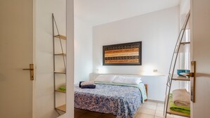 Une chambre à coucher avec un lit, une œuvre d’art accrochée au mur et une étagère avec des serviettes.