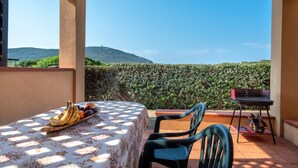 A balcony with a table set with fruits, a chair, and a grill.