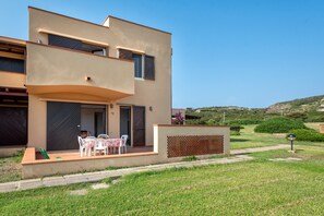 A modern two-story building with a flat roof, a balcony, and a small outdoor seating area with a table and chairs.
