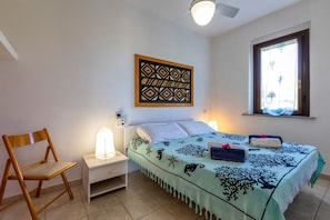 A bedroom with a bed, a nightstand, a chair, a ceiling fan, a window, and a wall decoration. - Holiday Home "Pergola 705" Just a Few Meters from the Beach with Private Terrace (STINTINO)