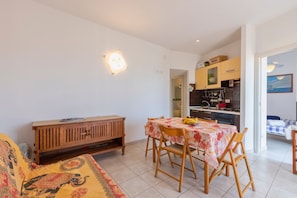 A dining area with a table and chairs, a wooden cabinet, and a kitchen visible through an open doorway. - Holiday Home "Pergola 705" Just a Few Meters from the Beach with Private Terrace (STINTINO)