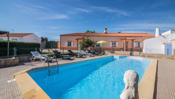 A swimming pool with lounge chairs and a statue, surrounded by a building with a tiled roof.
