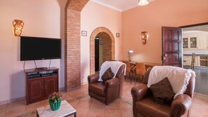 A living room with a TV, leather chairs, a coffee table with flowers, a brick archway, and a dining area in the background.