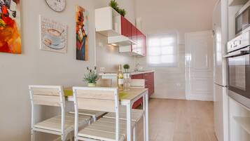 Een moderne keuken met witte kasten, een eethoek met een houten tafel en stoelen, en een koelkast.