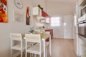 Una cocina moderna con armarios blancos, un comedor con mesa y sillas de madera, y un refrigerador.