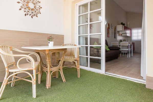 Ein Zimmer mit Esstisch, Stühlen, einer Topfpflanze und einer Glasschiebetür, die in einen Küchenbereich führt.