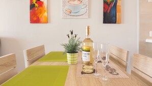 Een eettafel met een wijnfles, twee glazen, een potplant en een lijst met een kunstwerk aan de muur.