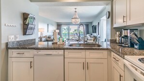A kitchen with granite countertops, white cabinets, a built-in dishwasher, and a chandelier.