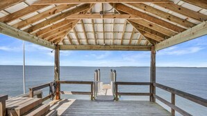 A wooden deck with a metal railing, leading to a covered area with a view of the sea.