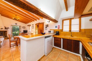 Een keuken met houten balken, een centraal eiland, een vaatwasser en een eethoek met een tafel en stoelen.