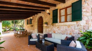 A stone-walled patio with wicker furniture, a wooden door, and a stone bench. - Holiday Home 'Can Pedro Monjo' with Private Pool, Private Terrace and Wi-Fi (Alcudia)