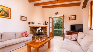 A living room with a fireplace, sofas, a television, and a view of the outdoors. - Holiday Home 'Can Pedro Monjo' with Private Pool, Private Terrace and Wi-Fi (Alcudia)