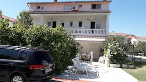 A two-story building with a balcony, a car parked in front, and outdoor seating. - Sunset View Rab Apartment (Rab)